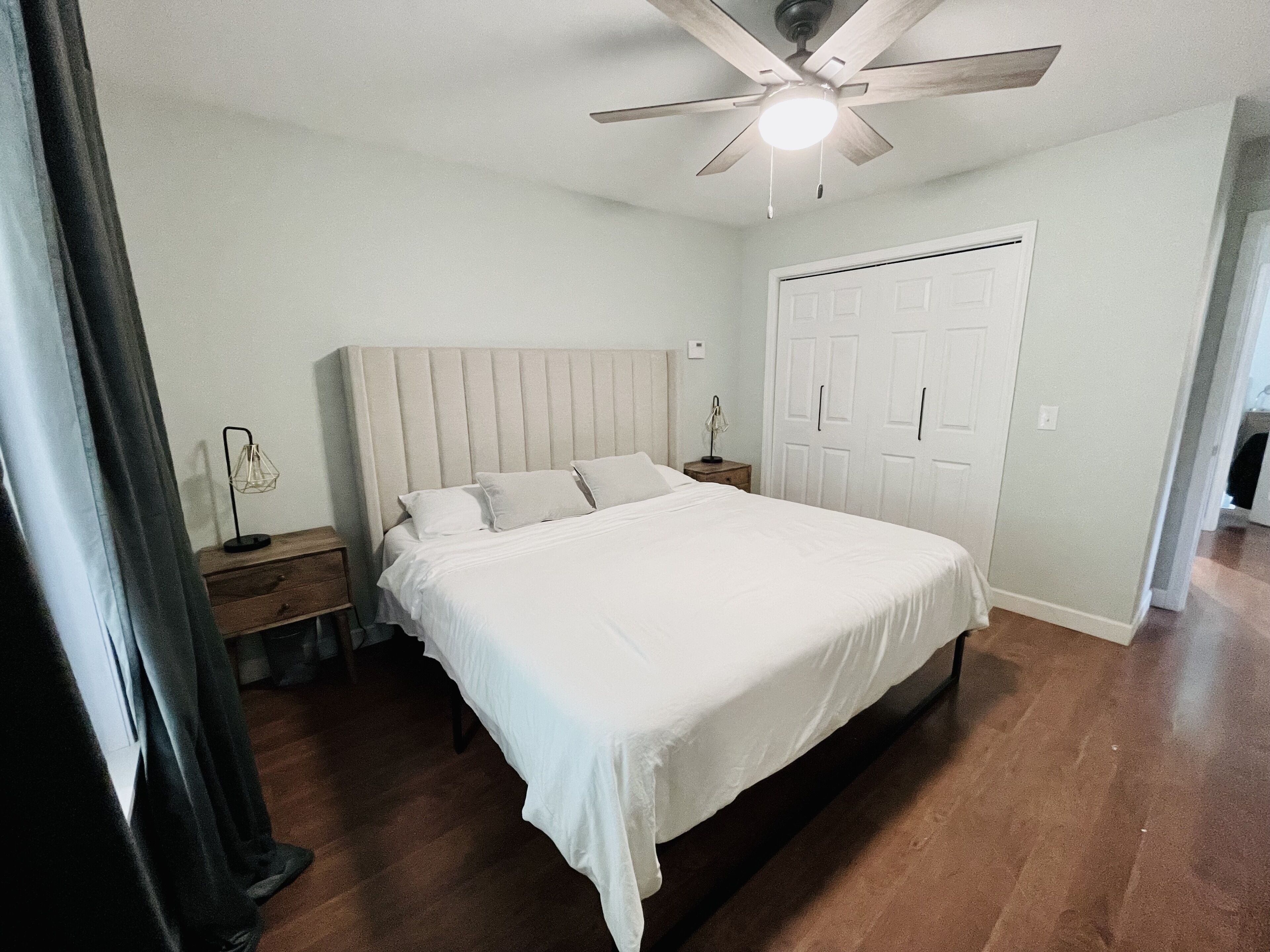 A bedroom with a bed, a ceiling fan, a nightstand, a lamp, and a wardrobe.