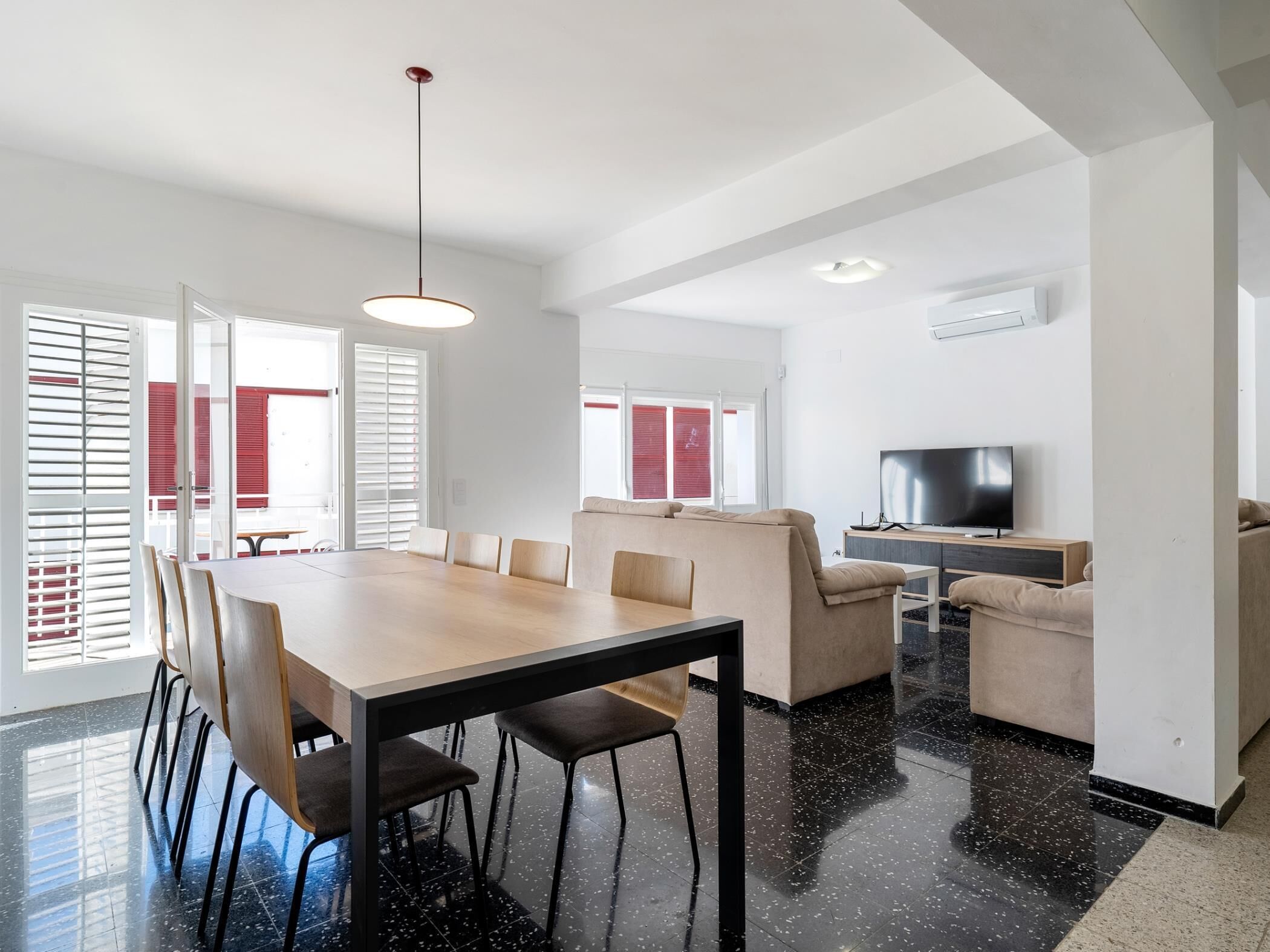 A modern living room with a dining area, a sofa, a TV, and a large window with blinds.