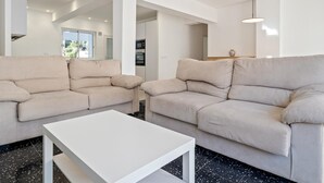 Un soggiorno moderno con due divani beige, un tavolino bianco e una cucina sullo sfondo.