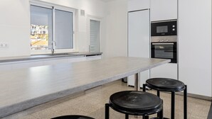 Una cucina moderna con mobili bianchi, un forno a microonde integrato e un forno. Due sgabelli neri al bancone.