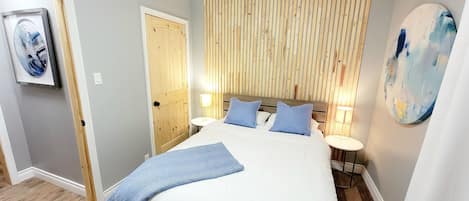 A bedroom with a bed, wooden panel wall, bedside lamps, and a painting.