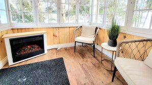 A cozy room with a fireplace, wicker chairs, and large windows offering a view of trees. - Top 5% • 3BR Gem • Prime Location, Special Backyard, Great Hosts  (Huntsville)