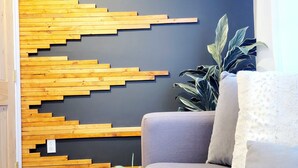 A modern living room with a wooden slat wall design, a grey sofa, a white cushion, a small potted plant, and a coffee table with a cup and saucer. - Top 5% • 3BR Gem • Prime Location, Special Backyard, Great Hosts  (Huntsville)