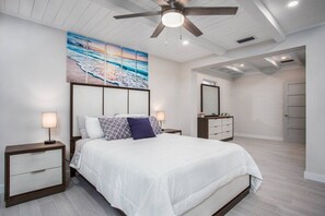 A bedroom with a bed, nightstands, a ceiling fan, a painting, and a walk-in closet.