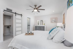 A bedroom with a bed, a ceiling fan, a dresser, a mirror, and a door leading to a closet. - Sunkissed Pool Home, Fully Renovated, Pet Friendly (Siesta Key)