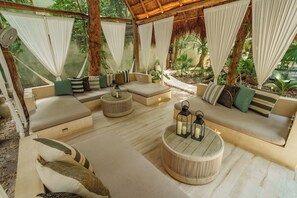A cozy outdoor seating area with cushioned sofas, a round coffee table, and hanging curtains. - Terasu Riviera Maya Hotel & Spa Luxury Edition, en Xcaret (Playa del Carmen)