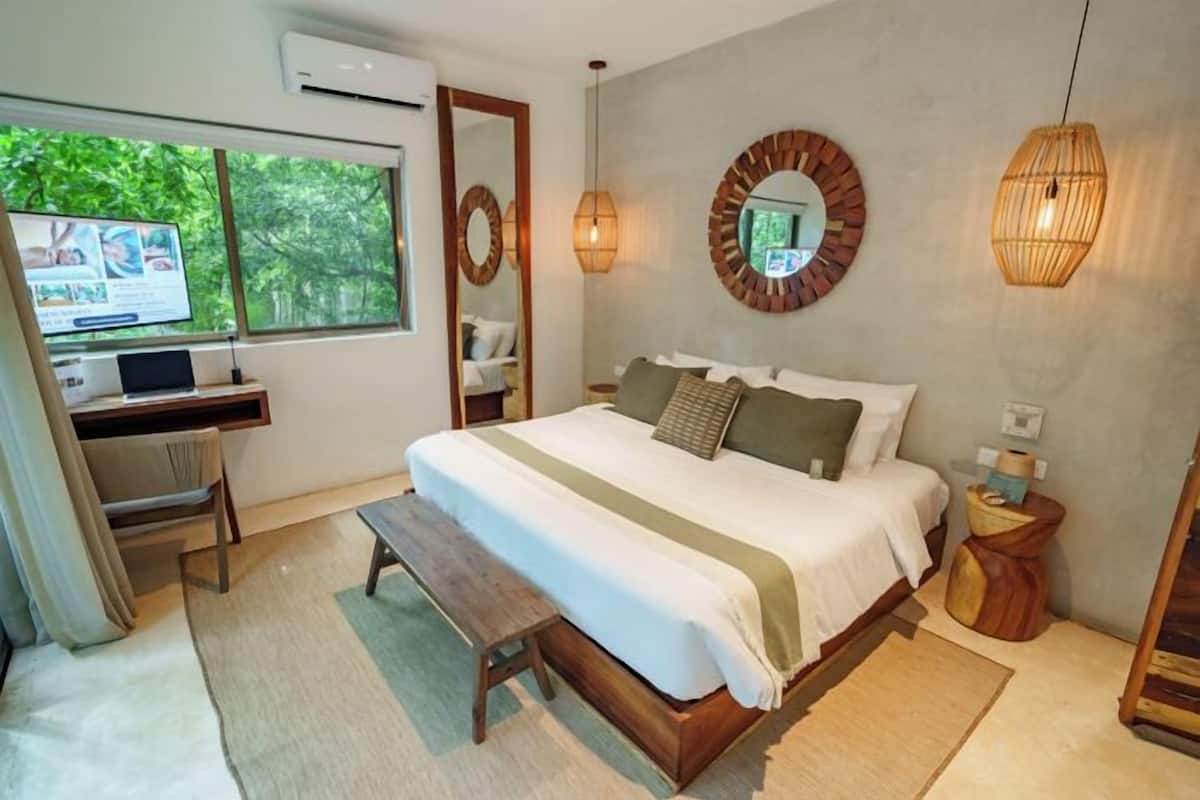 A bedroom with a bed, desk, computer, and a large window.
