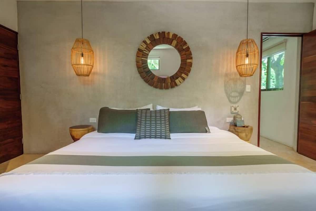 A bedroom with a large bed, two wall-mounted lamps, a circular mirror, and a wooden side table.