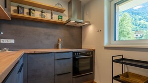 A modern kitchen with a wooden countertop, built-in oven, and a window with a view of a forested area. - Small, charming, centrally located and yet quiet (Bad Hofgastein)