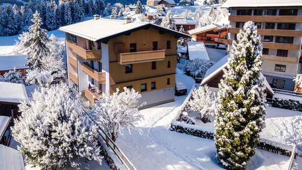 A multi-story building with balconies, surrounded by snow-covered trees and mountains in the background. - Small, charming, centrally located and yet quiet (Bad Hofgastein)