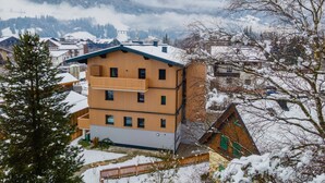 A multi-story building with a balcony, surrounded by snow-covered trees and mountains in the background. - Small, charming, centrally located and yet quiet (Bad Hofgastein)