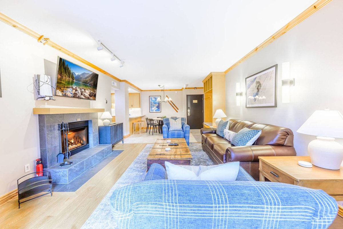 Ein modernes Wohnzimmer mit Kamin, einer Ledersofa, einem Couchtisch und einem an der Wand befestigten Fernseher.