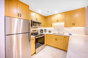 A modern kitchen with stainless steel appliances, wooden cabinets, and a white countertop.
