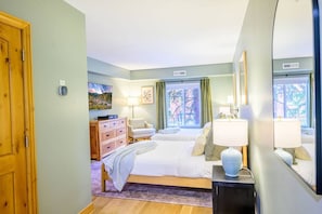 A hotel room with a bed, bedside tables, a dresser, a chair, and a window with curtains.