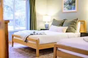 A neatly made bed with a blanket and pillows, a bedside table with a lamp, and a window with curtains.