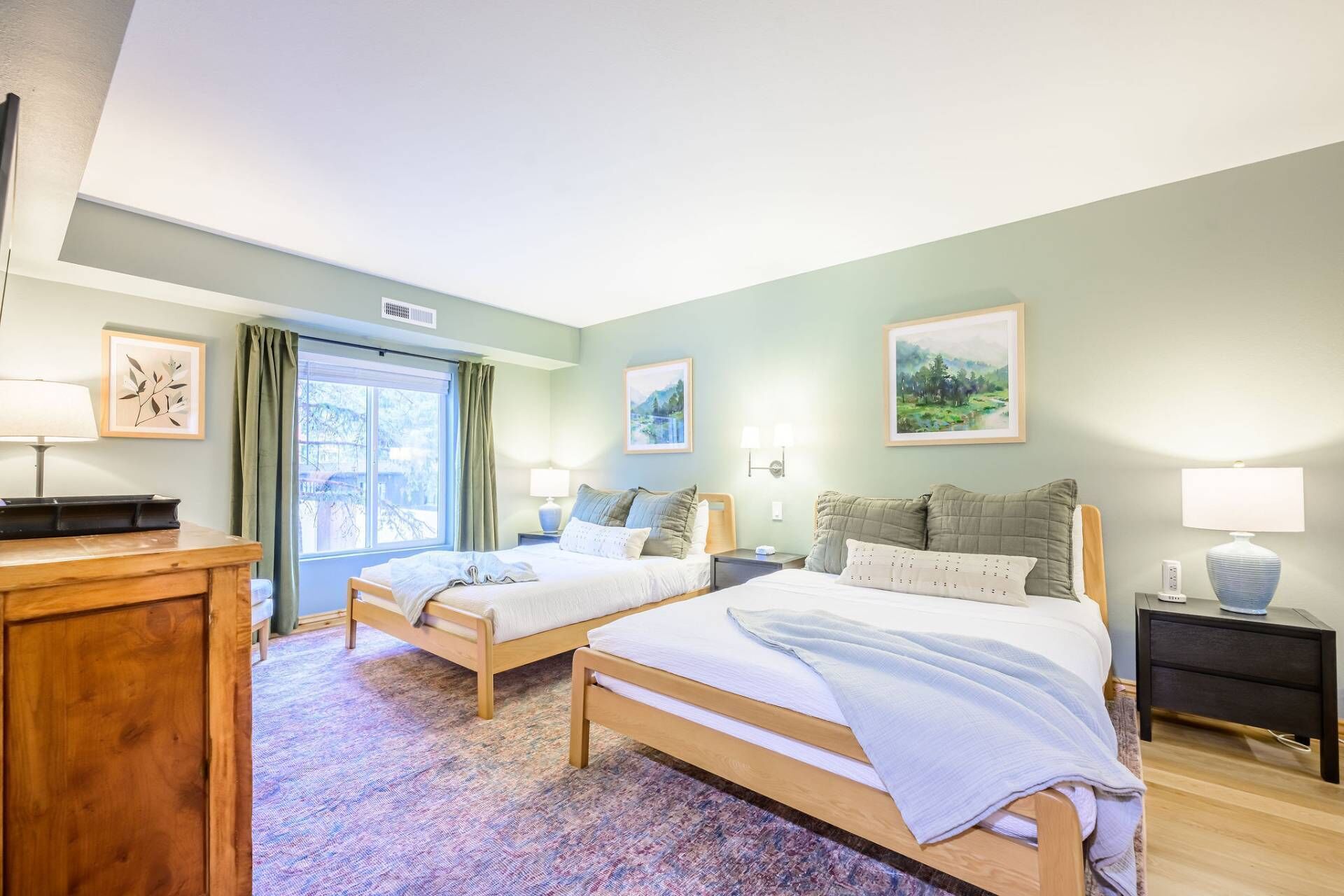 Een hotelkamer met twee bedden, een houten dressoir, een bureau en een raam met gordijnen.