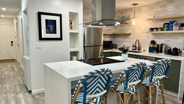 Una cocina moderna con una isla central, taburetes de bar, electrodomésticos de acero inoxidable y un salpicadero de azulejos.