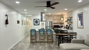 Una cocina moderna con una isla central, taburetes de bar y una zona de comedor con sofá.