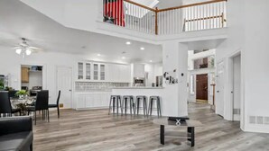 Een ruime woonkamer met hoge plafonds, een eethoek en een keuken met witte kasten en een centraal eiland.