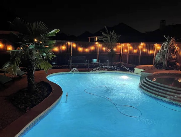 A swimming pool at night with surrounding lights and a mountain in the background.