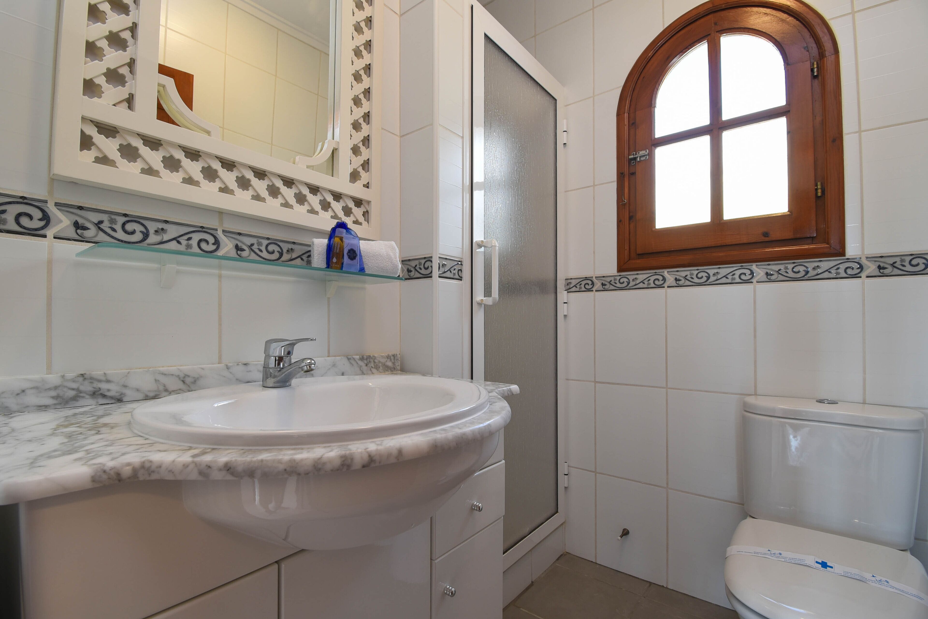 Une salle de bain avec un lavabo en marbre, des toilettes, une douche et une fenêtre avec un cadre en bois.