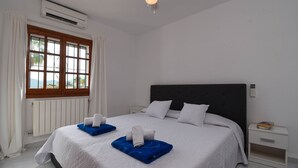 Une chambre d’hôtel comprenant un lit, une table de chevet, un climatiseur, une fenêtre avec des rideaux et un ventilateur de plafond.