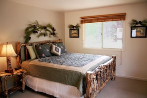 A bedroom with a bed, a nightstand, a window with blinds, and wall decorations.
