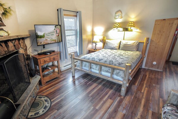 A bedroom with a wooden bed, a television, a fireplace, and a window with curtains.