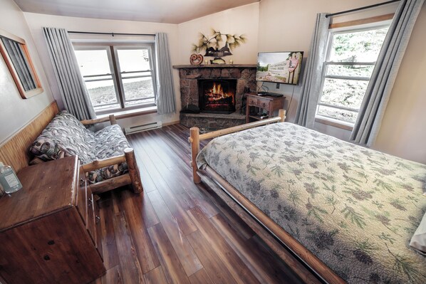 A cozy room with a fireplace, wooden furniture, and large windows.