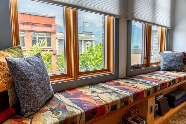 A window seat with a colorful cushion, a view of a building, and a bookshelf with books.