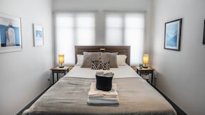 A neatly made bed with a folded towel, two bedside lamps, and a headboard.