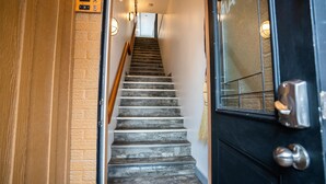 Una escalera que lleva a un cuarto con una puerta negra, un muro de madera y un accesorio de luz.