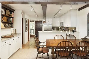 A modern kitchen with white cabinetry, a stainless steel refrigerator, and a dining area with a wooden table and chairs.