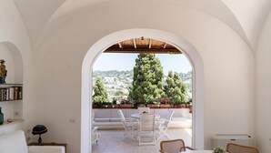 A room with a white arched doorway leading to an outdoor seating area with a view of a cityscape and trees. - Villa Birago in Capri (Capri)