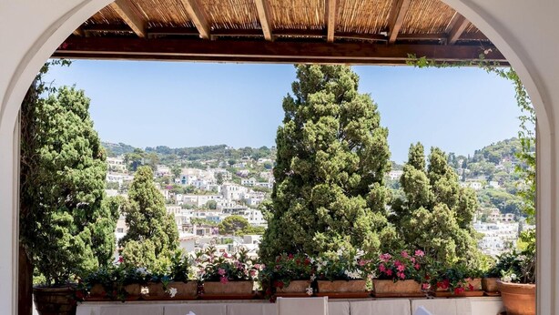 An outdoor patio with a round table and chairs, a cushioned bench, and potted plants. - Villa Birago in Capri (Capri)