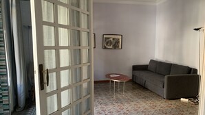 Ein Wohnzimmer mit grauem Sofa, einem kleinen runden Tisch, einem gemusterten Teppich und einer Tür mit Glasfenstern.