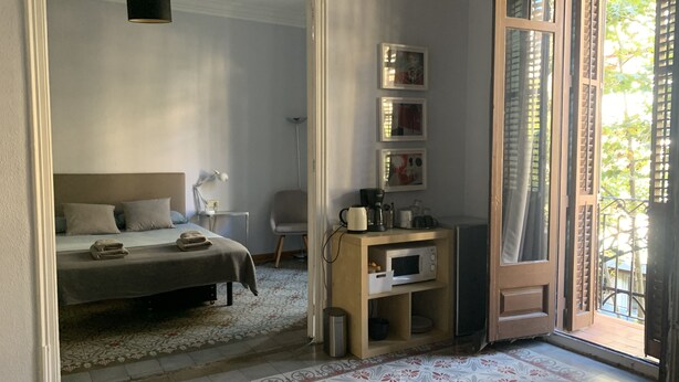 Ein Schlafzimmer mit Bett, Nachttisch, Lampe und Blick durch eine offene Tür auf einen Balkon.