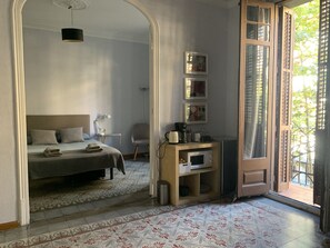 A bedroom with a bed, bedside table, lamp, and a view through an open door to a balcony. - Art nouveau suite in Eixample building! (barcelona)