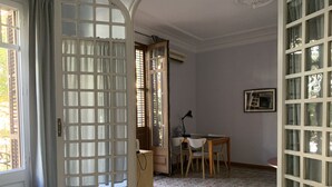 Ein Zimmer mit einem Bett, einem Schreibtisch und einem Stuhl. Es gibt ein Fenster mit Vorhängen und eine Tür mit Fensterteil.