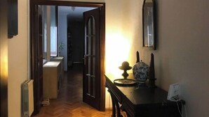 Ein Korridor mit Holzboden, einem Heizkörper, einer Tür zu einem anderen Raum, einem Tisch mit Lampe und einem Spiegel an der Wand.