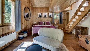 L’intérieur d’un chalet en bois, avec un lit, un canapé, un escalier et une vue sur l’extérieur.