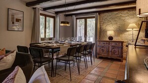 Un espace repas agrémenté d’un mur en pierre rustique, de poutres en bois et d’un lustre.