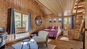 Une chambre confortable dans un chalet en bois, avec un lit, une chaise, une petite table, une cheminée et une fenêtre avec des rideaux.