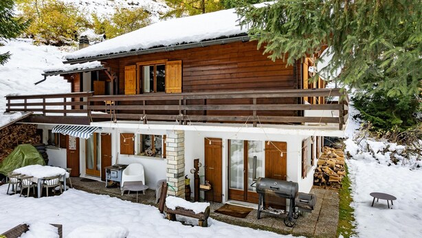 Une cabane en bois dotée d’un patio couvert, d’un espace barbecue et d’une terrasse recouverte de neige.