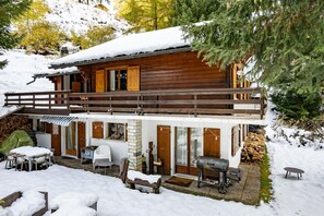 Una cabaña de madera con un porche cubierto, una zona de barbacoa y una terraza nevada.
