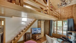 L’intérieur d’un chalet en bois comprend un lit, un téléviseur, une cheminée et un escalier.