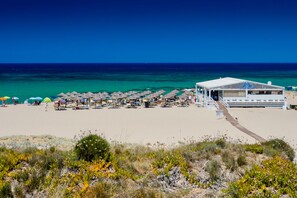 A beach with a white building, rows of umbrellas, and a clear blue sky. - Villa Natalka with garden in Valledoria (Valledoria)