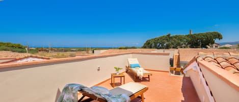 Una terraza en la azotea con vistas despejadas al mar, una silla de descanso, una mesita con una planta y suelo de baldosas.