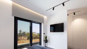 A modern bedroom with a large window, a bed, a potted plant, and a mounted TV. - Horizon Villa Oasis, Walk to Platanias Beach! (Chania)