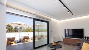A modern living room with a large flat-screen TV, a sofa, and a dining area with chairs and umbrellas. - Horizon Villa Oasis, Walk to Platanias Beach! (Chania)